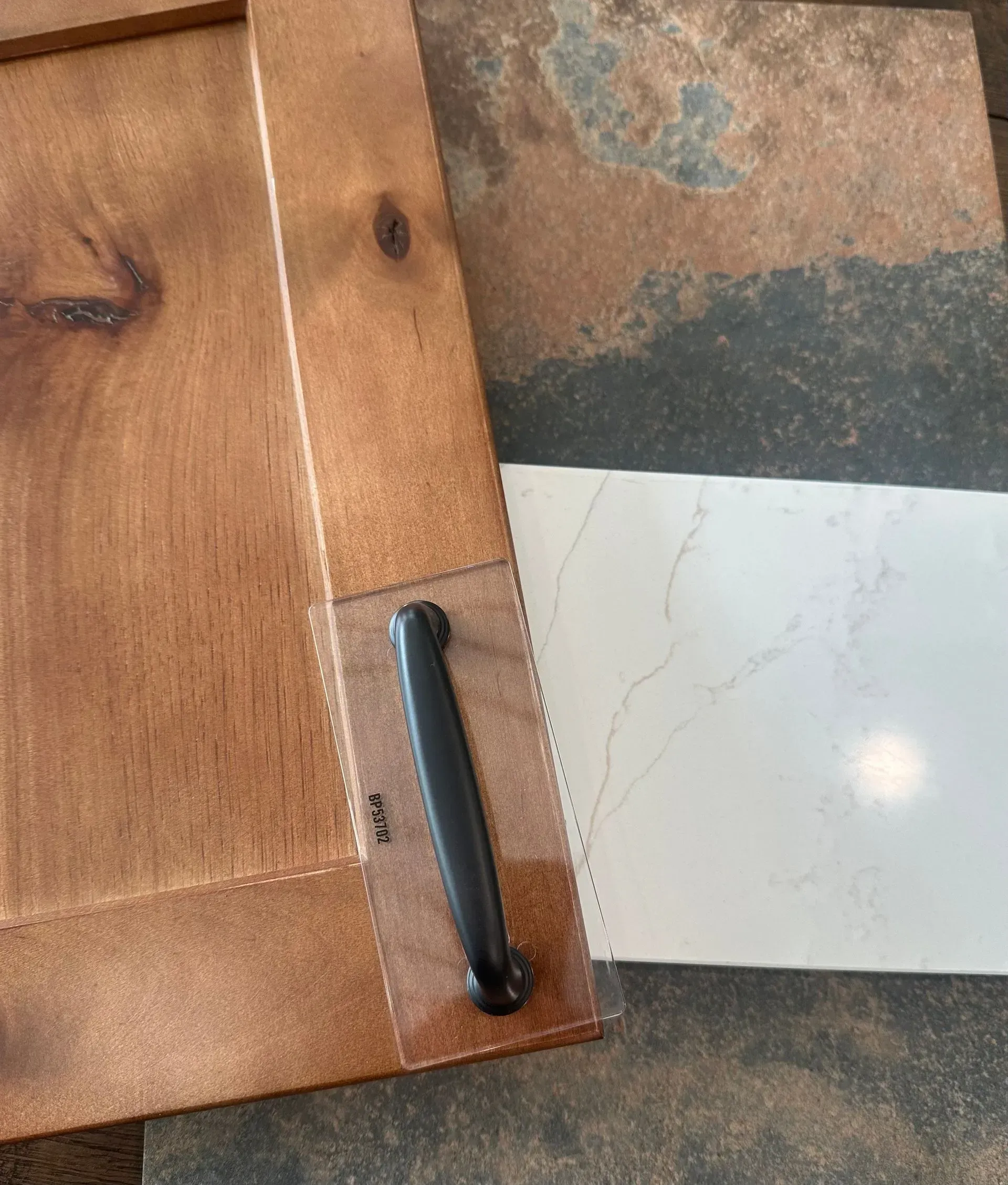 Cabinet door with black handle and white countertop sample on a mottled surface.