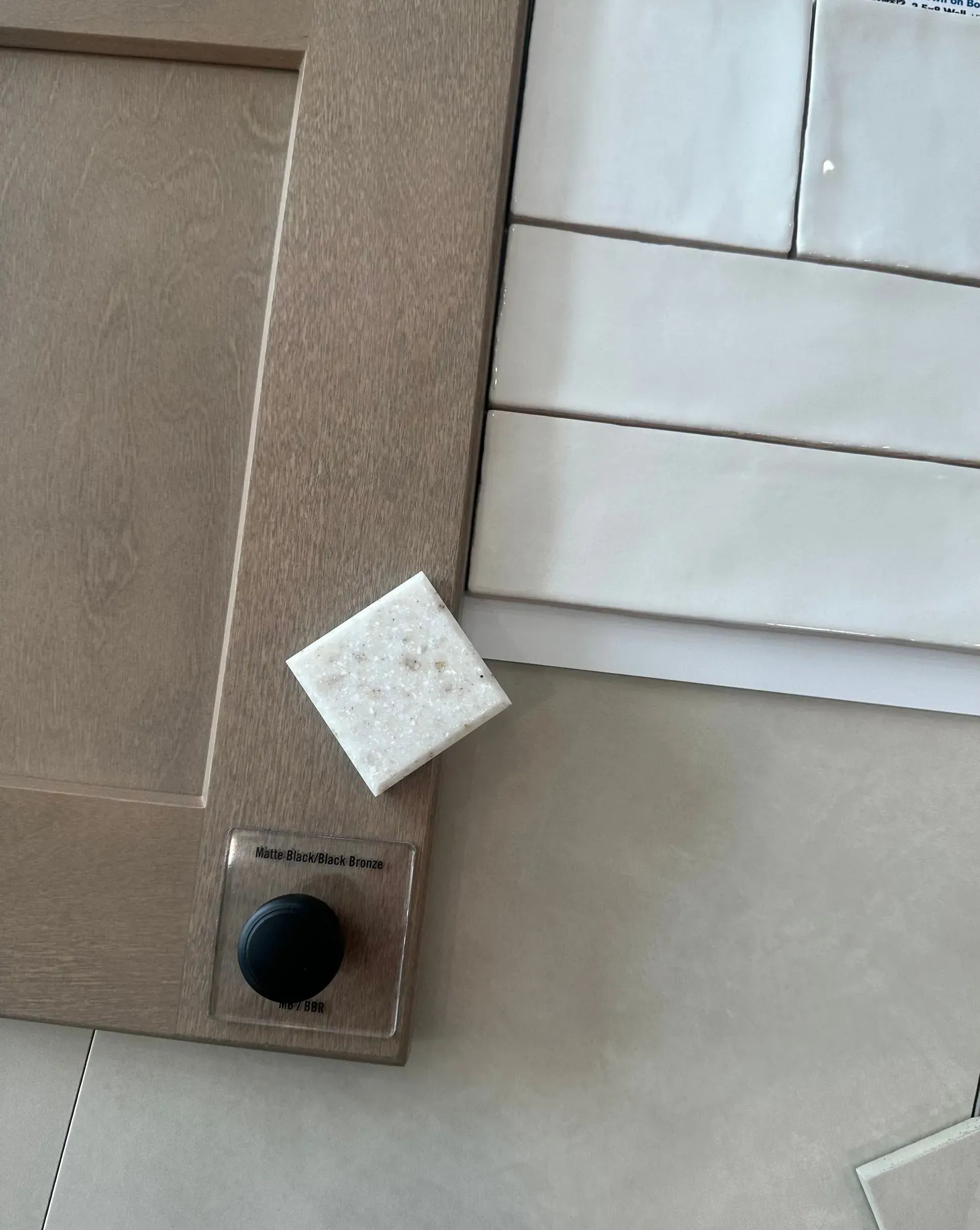 Close-up of a cabinet door with a square tile sample and other tiles, showing kitchen design options.