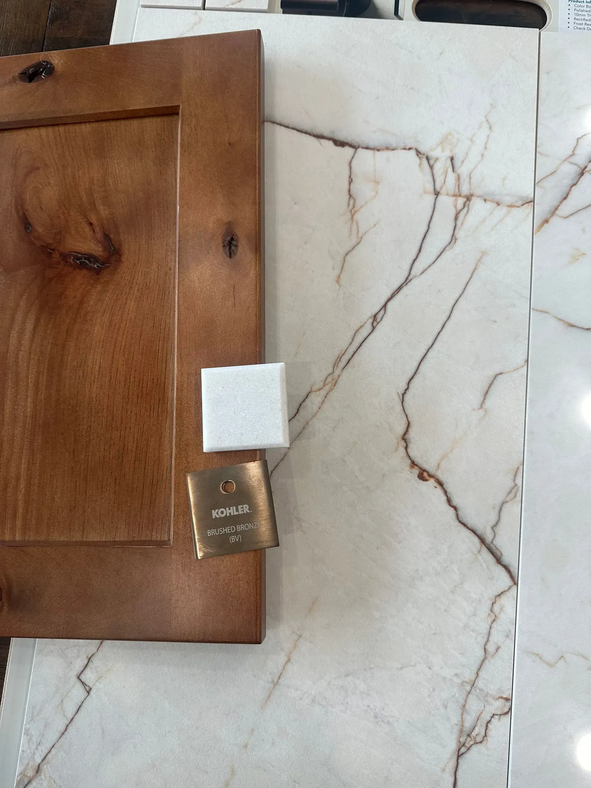 Wooden cabinet door next to marble countertop; brass hardware sample and white foam cube.