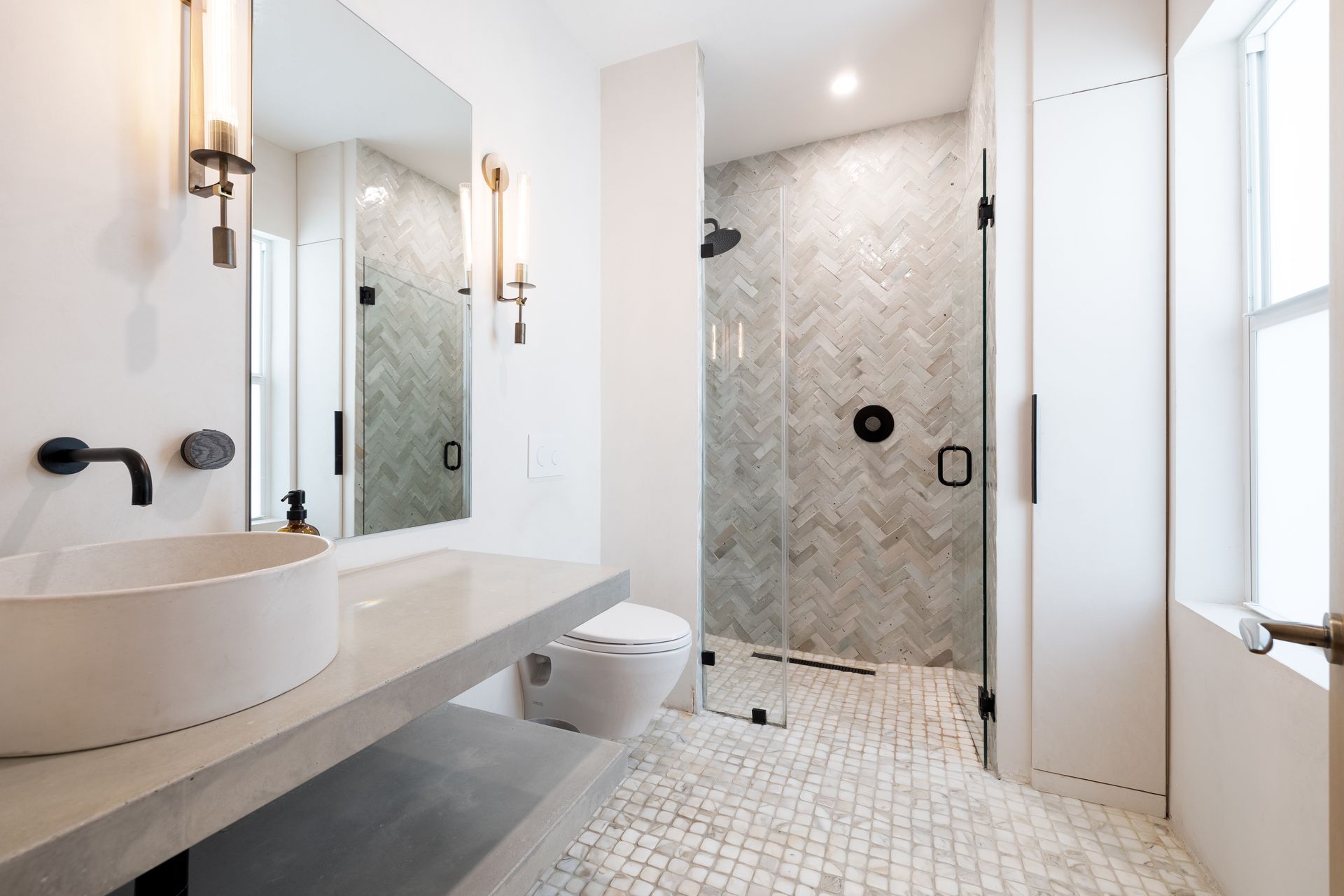 Modern white bathroom with a shower, sink, and toilet. Gray and white tile, black fixtures.