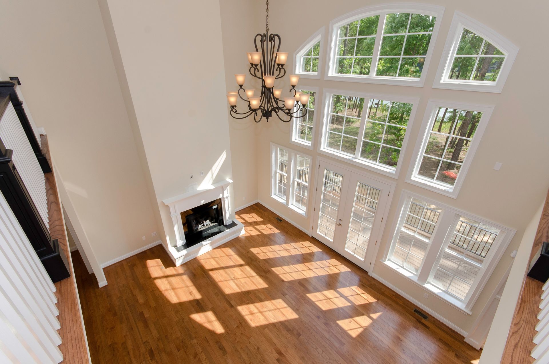Spacious living room with fireplace, large windows, and a chandelier. Sunlight streams across the hardwood floor.