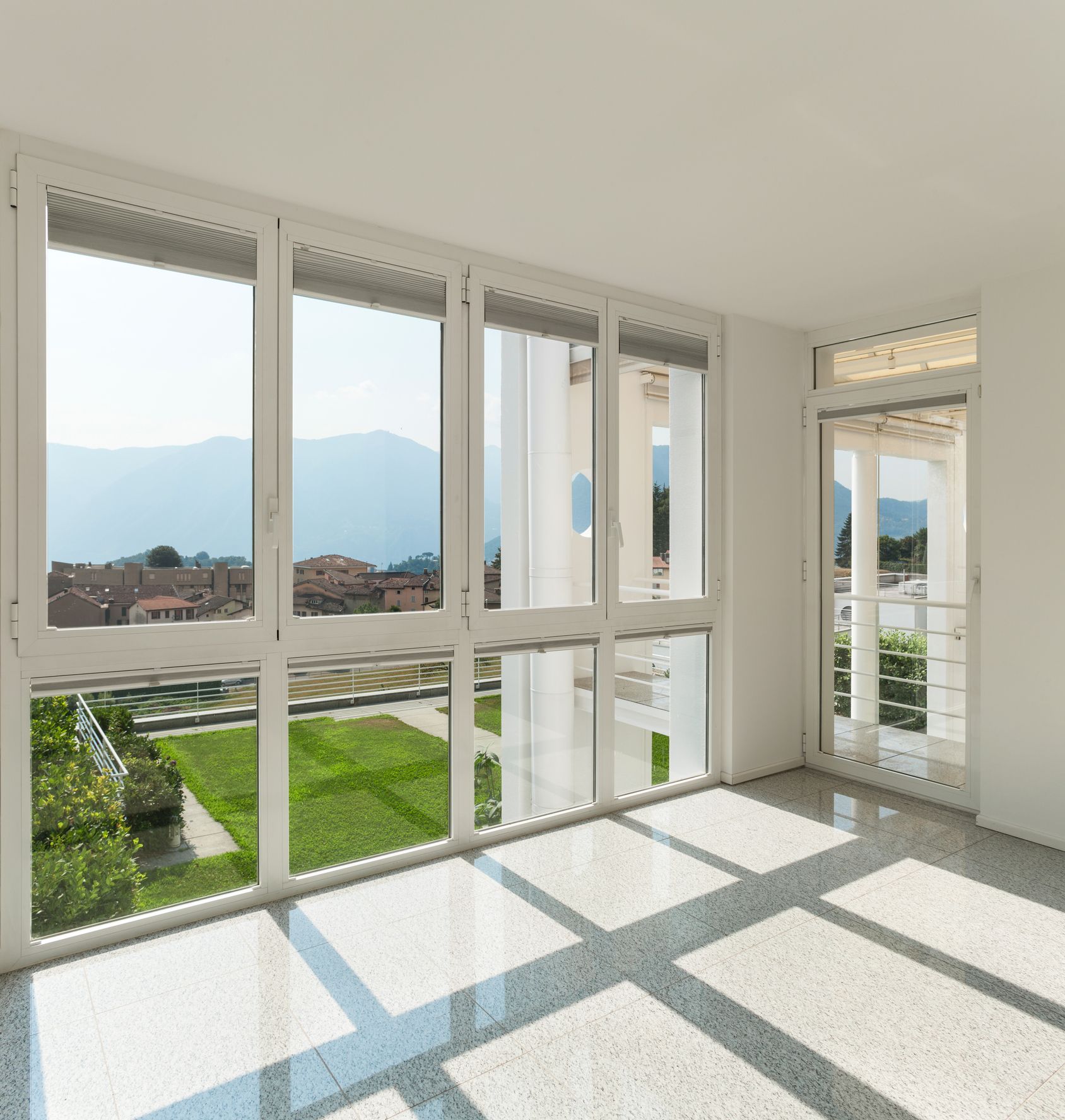 Empty sunlit room with large windows, city and mountain view.