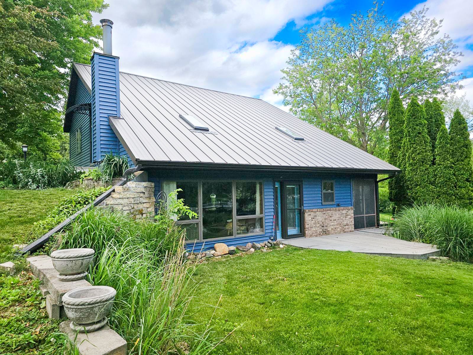 Blue house with metal roof, stone accents, and green lawn by Cedar Rapids siding company.