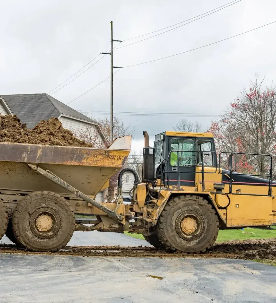 A dump truck is driving down a dirt road next to a house.