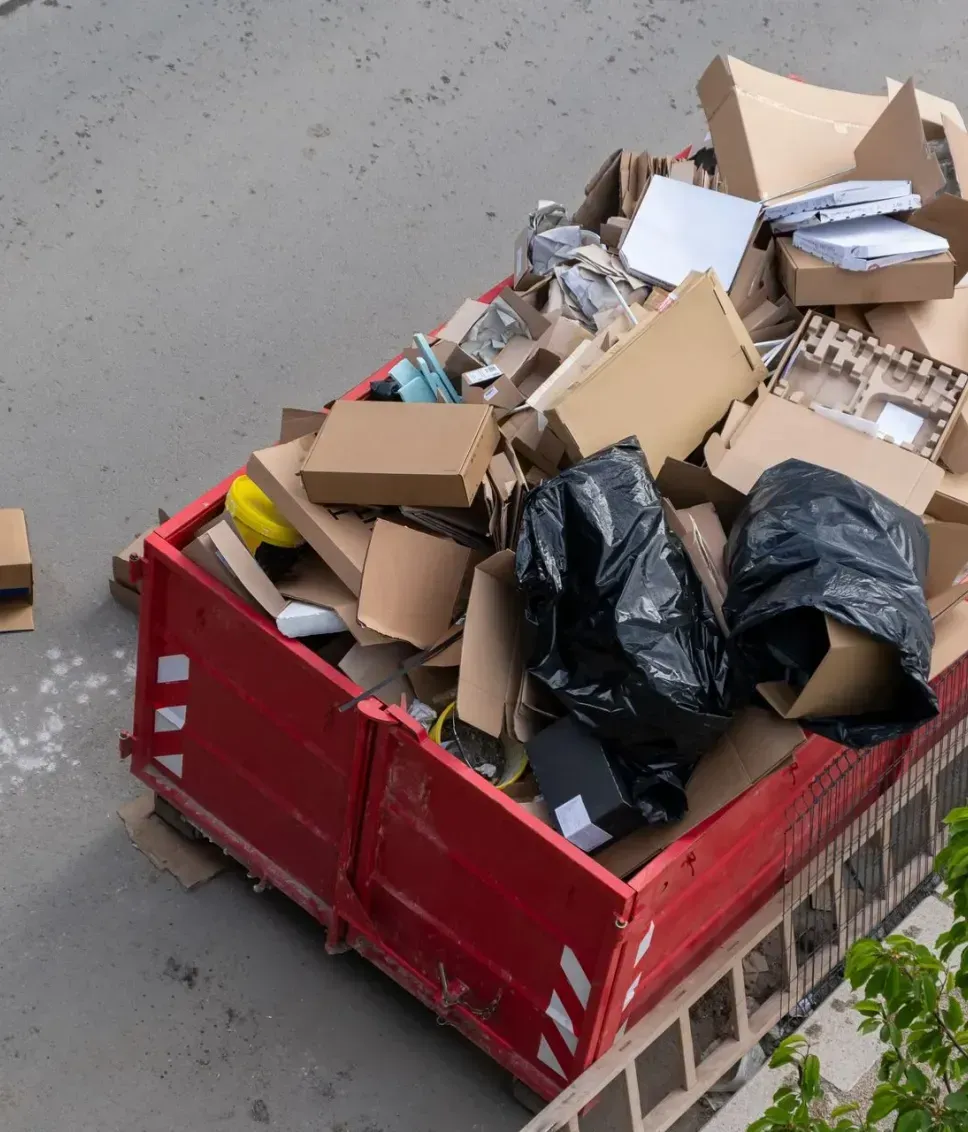 A red dumpster filled with cardboard boxes is sitting on the side of the road.