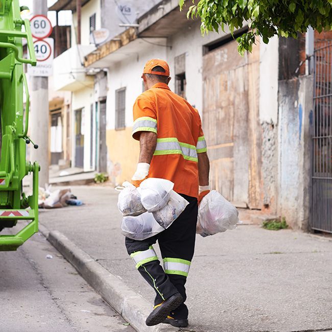 A man is walking down the street carrying bags of trash