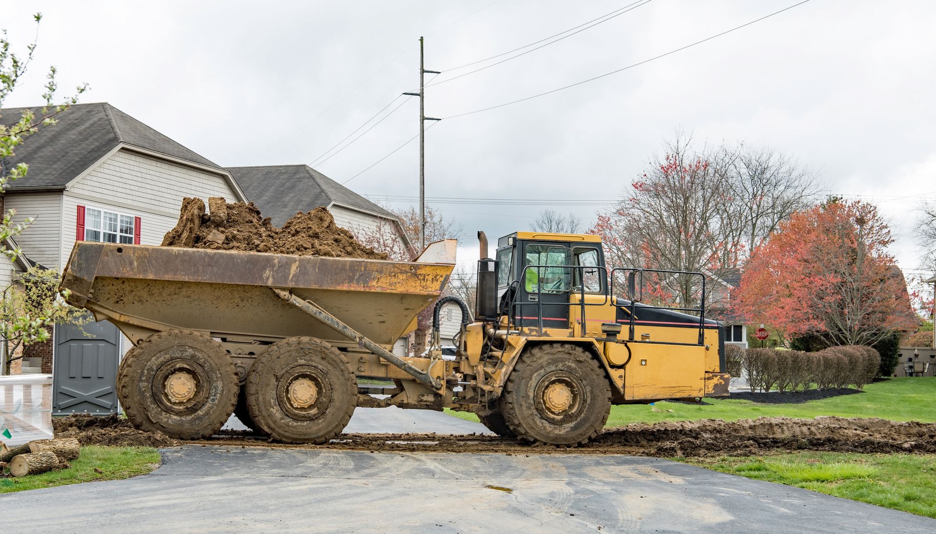 A dump truck is driving down a dirt road next to a house.