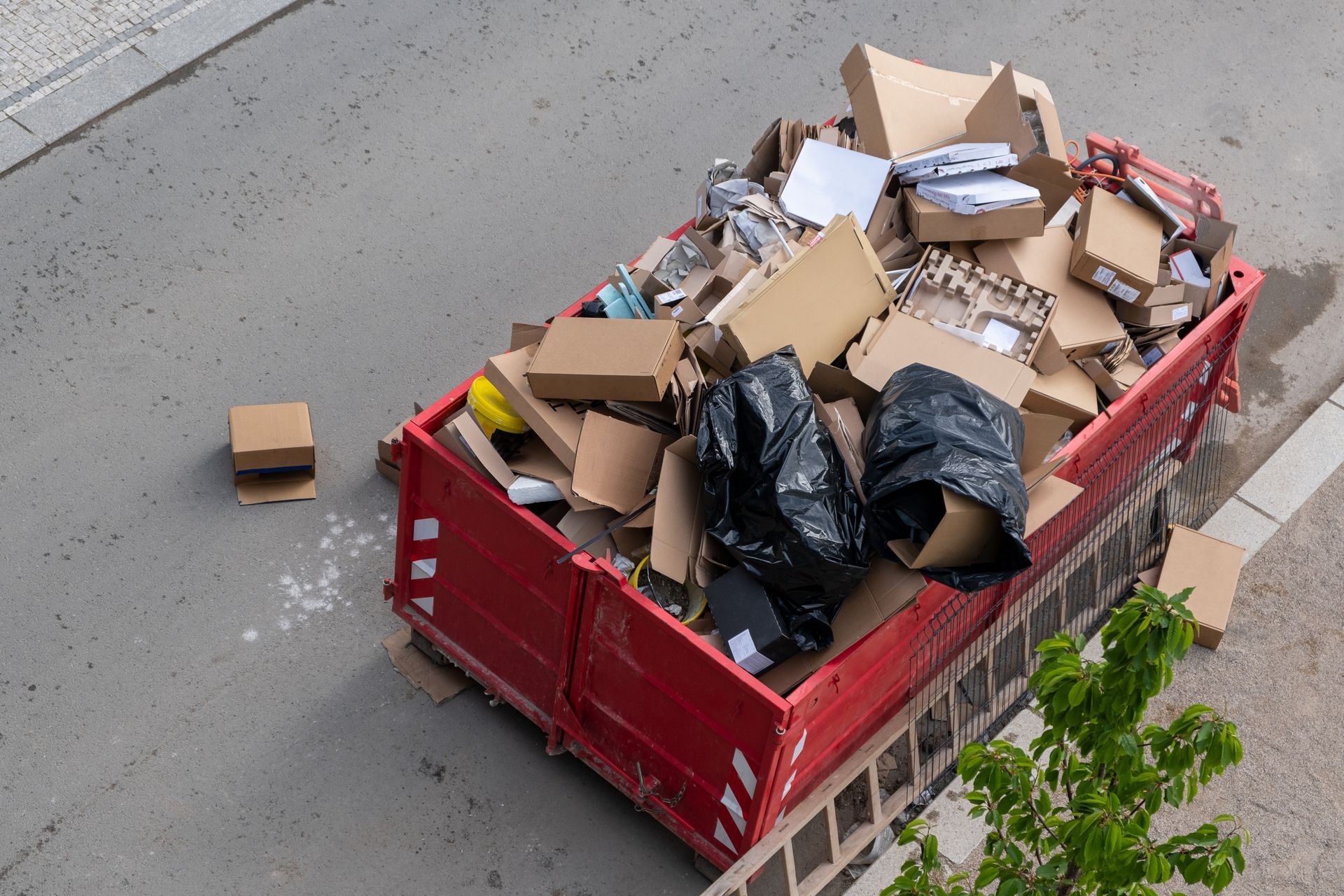 A red dumpster filled with cardboard boxes is on the side of the road.