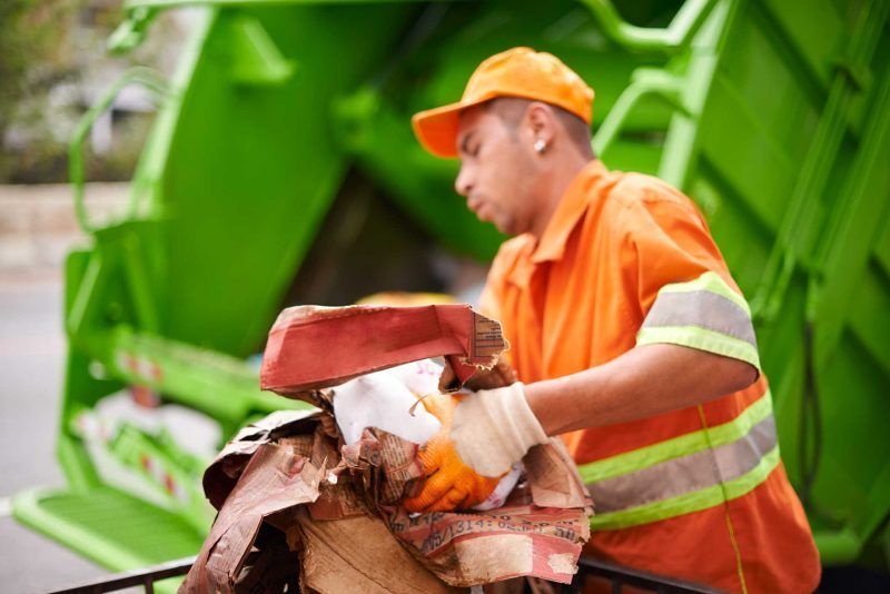 A man is loading garbage into a garbage truck.