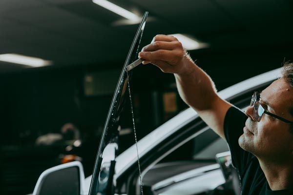 Mechanic inspecting a car windshield with a thin tool in a dim garage