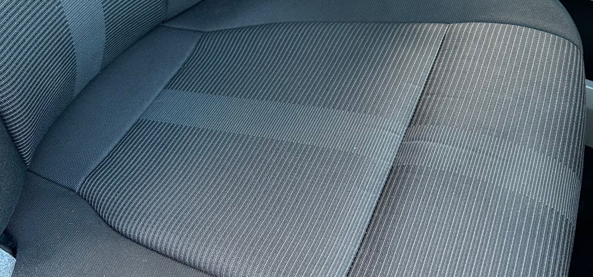 A close-up view of a dark gray textured fabric car seat with a repeating pattern of light-colored dots.
