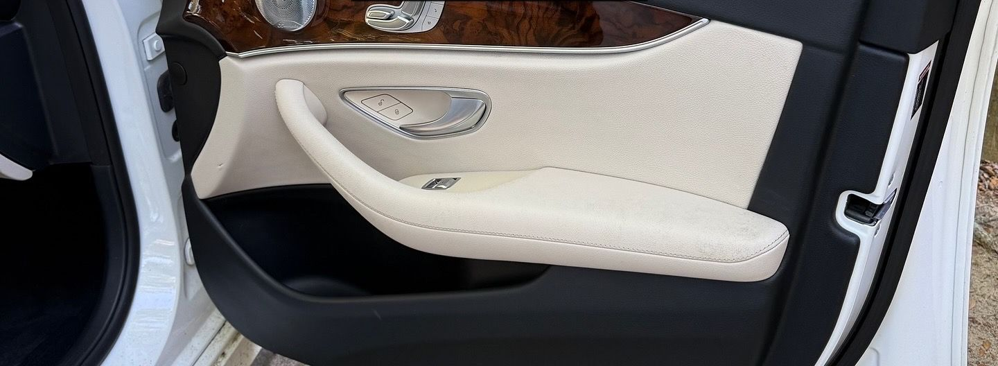 Interior door panel of a Mercedes-Benz vehicle featuring cream leather upholstery, wood trim, and a metal door handle.