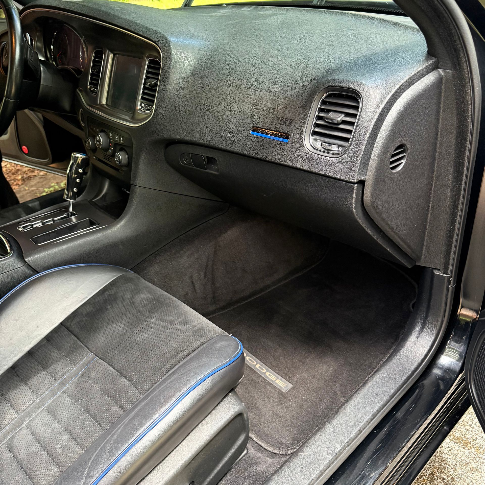 The interior of a black car with gray upholstery, blue stitching, and a textured dashboard.