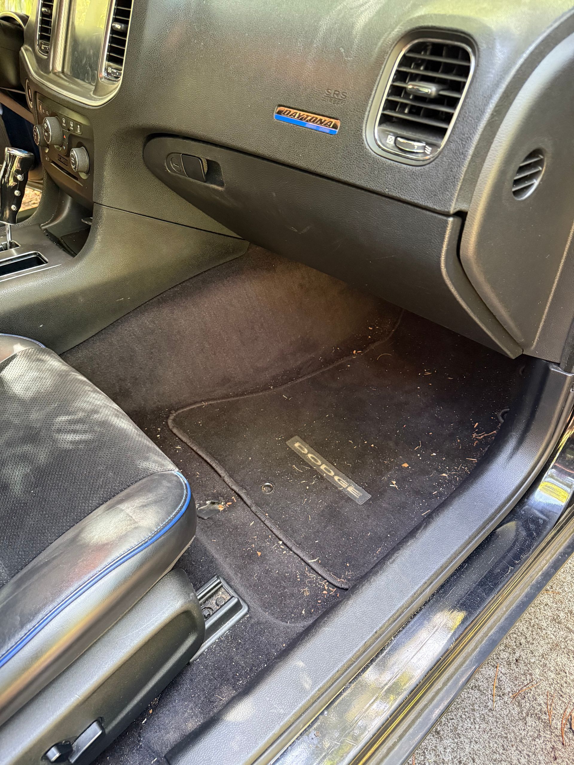 A view into a car’s passenger side, showing a dirty dashboard and floor mat covered in light-colored debris and dust.