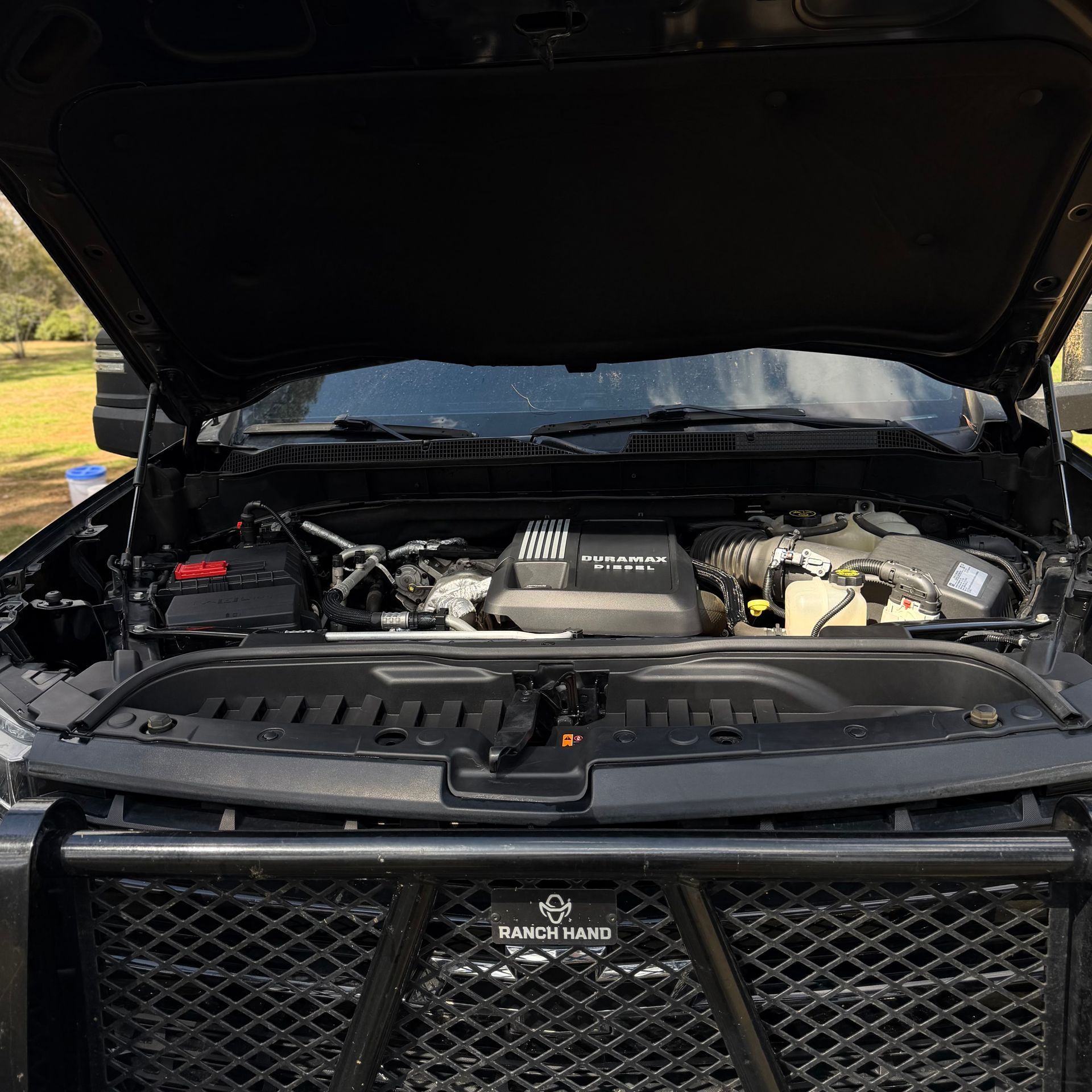 The open hood of a black truck reveals its engine bay, with a Ranch Hand grille guard visible in the foreground.