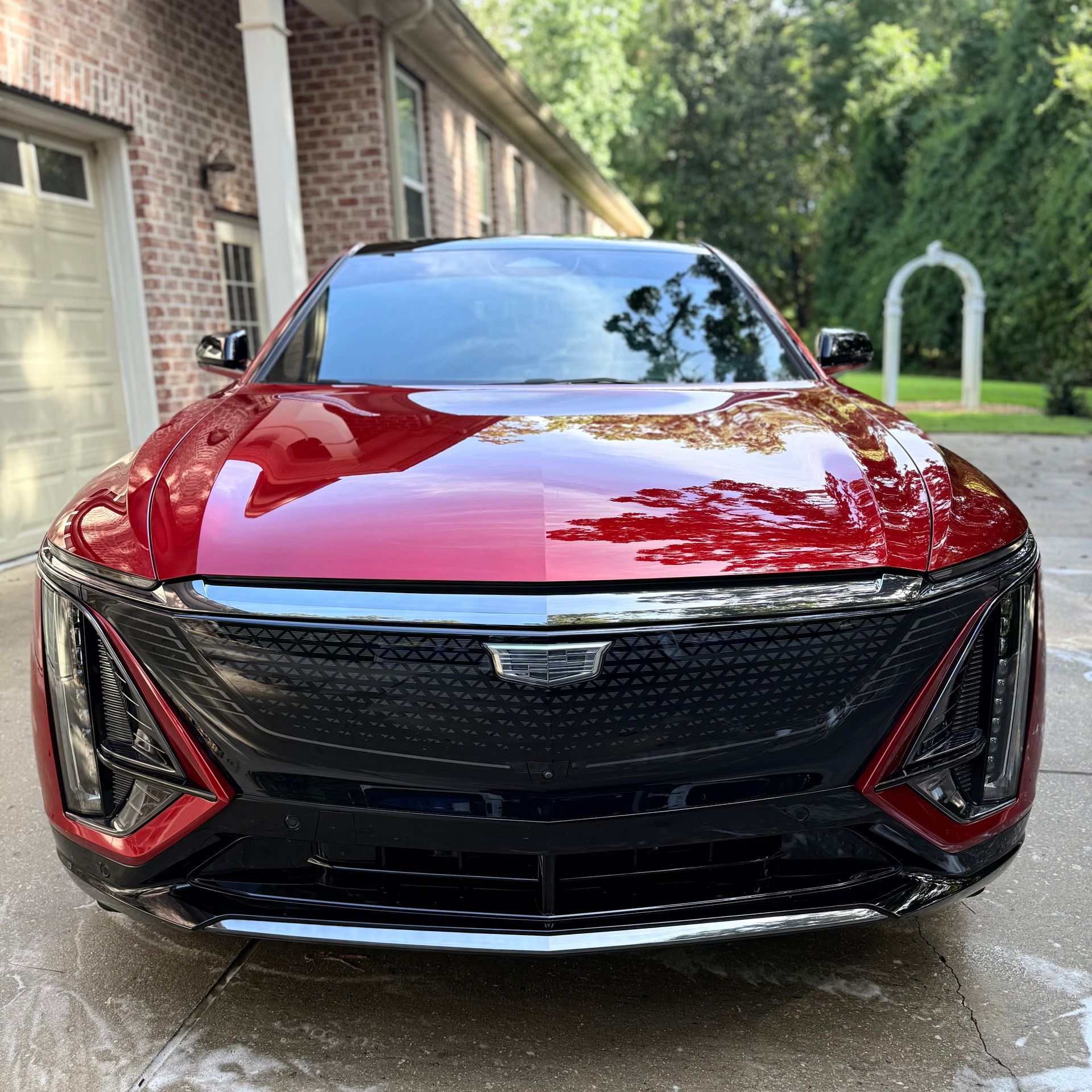 A gleaming, deep red Cadillac Lyriq electric SUV parked in a residential driveway, front-facing view.