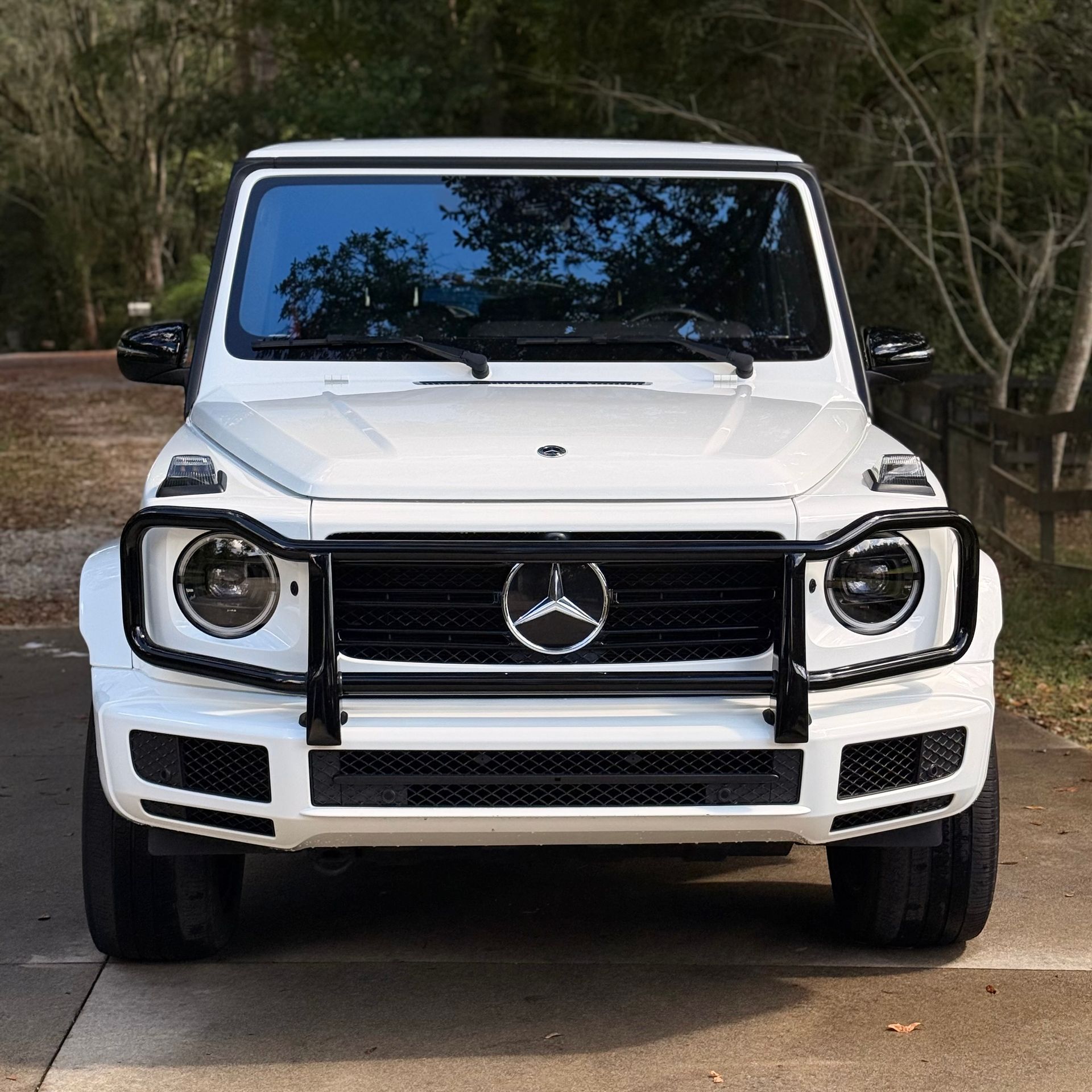 White Mercedes-Benz G-Class SUV front view on a driveway with trees in the background