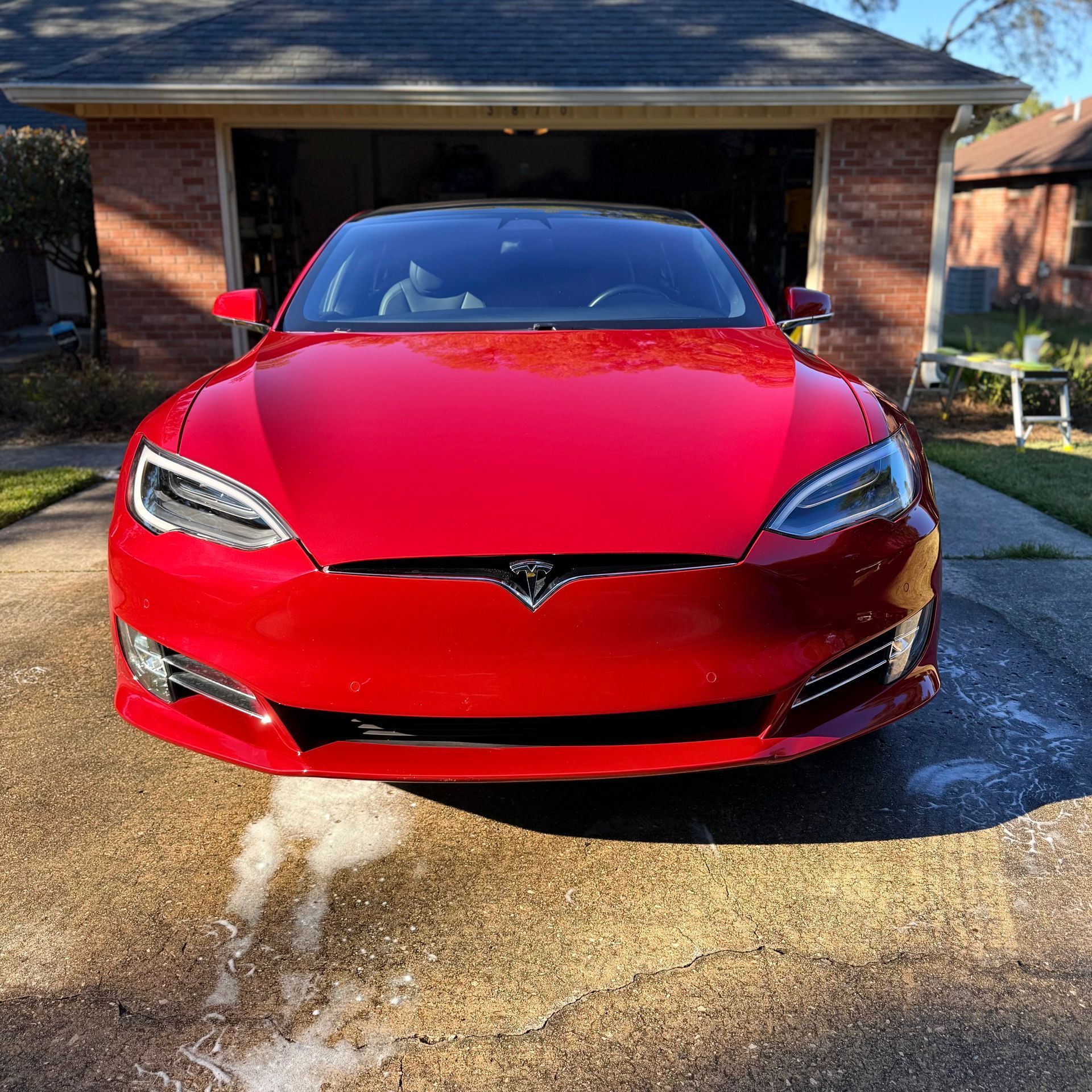 A shiny red Tesla Model S parked on a driveway in front of a brick house.