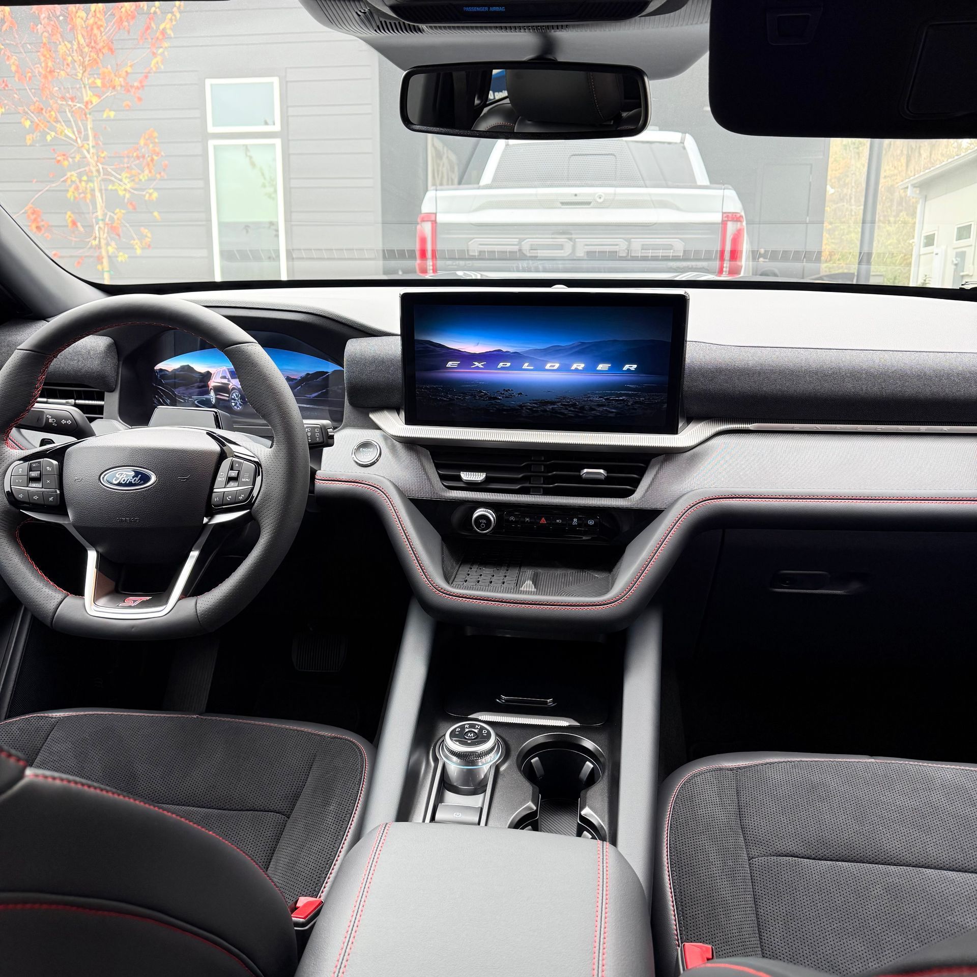 Interior view of a Ford Explorer with a digital screen, black upholstery with red stitching, and a rotary gear shifter.