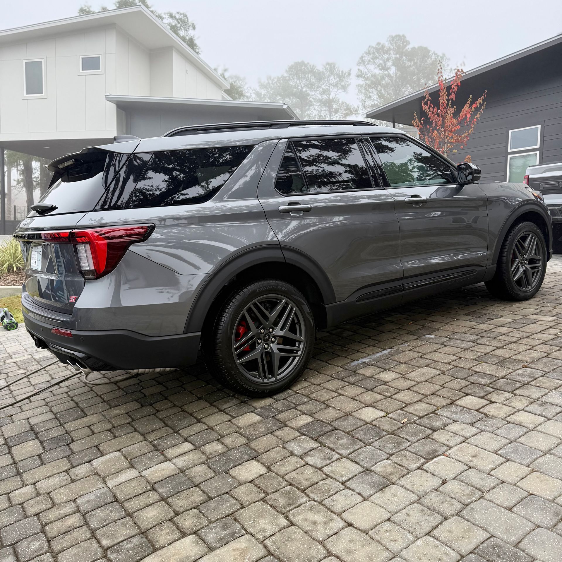 A gray SUV parked on a paved driveway in front of modern houses on a foggy day.