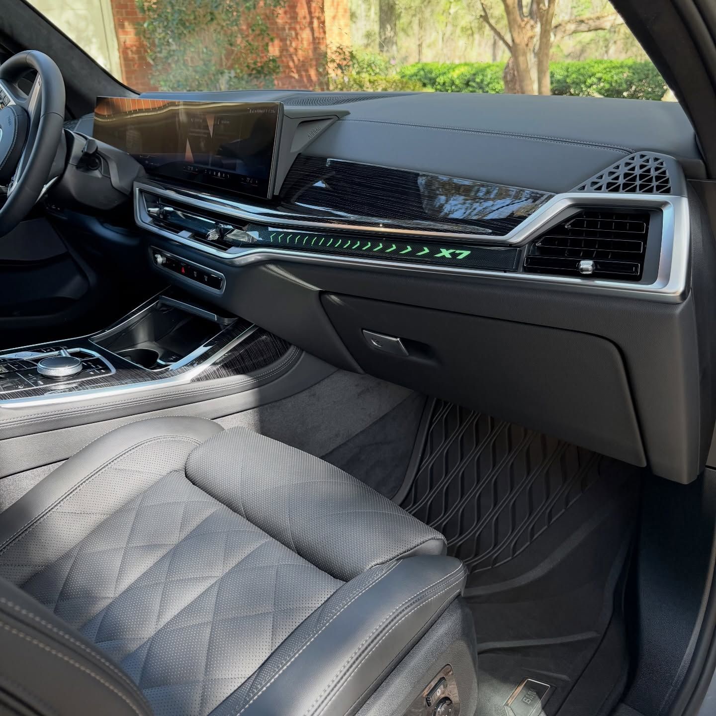 The interior of a modern BMW X7 featuring a large curved dashboard display, diamond-stitched leather seats, and floor mats.