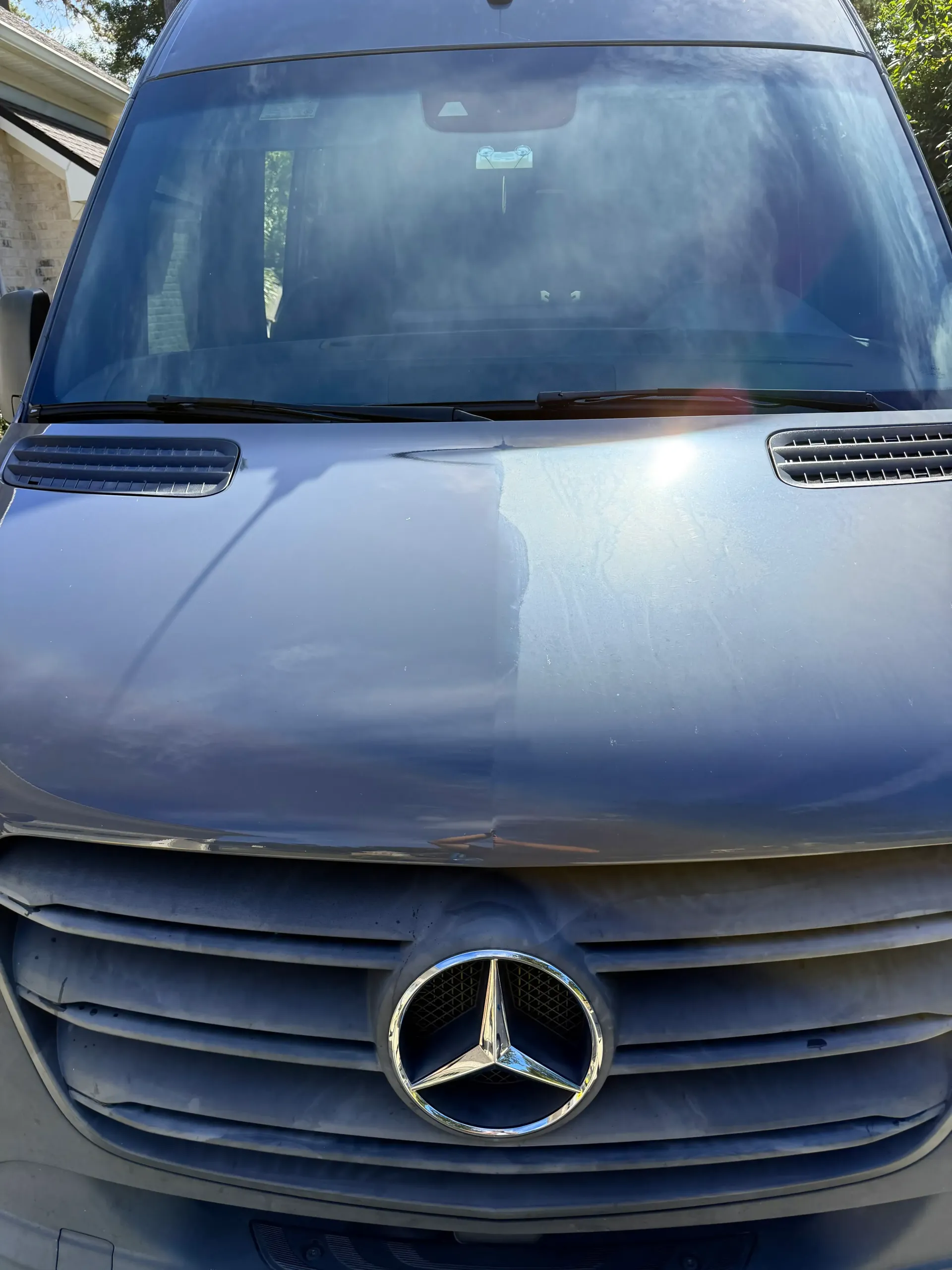 The front view of a grey Mercedes-Benz Sprinter van showing a distinct color difference between the two sides of the hood.