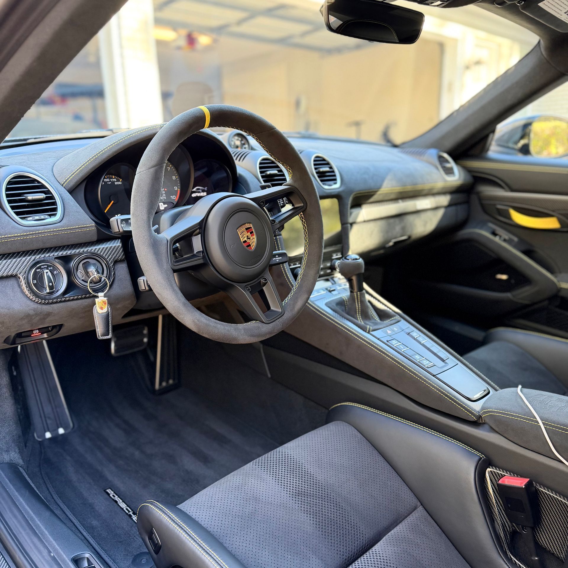 Interior of a modern Porsche sports car with a grey Alcantara steering wheel, dashboard, and bucket seats.