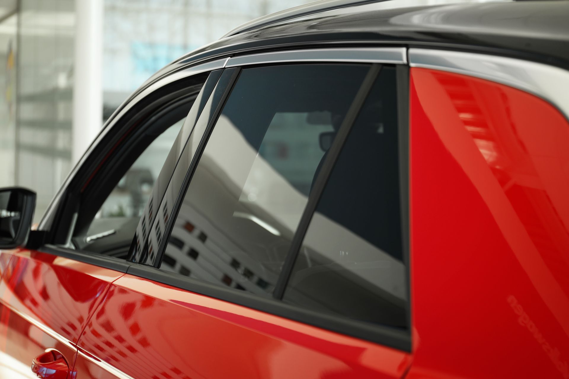 Red car side window with dark tinted glass and reflections of buildings.