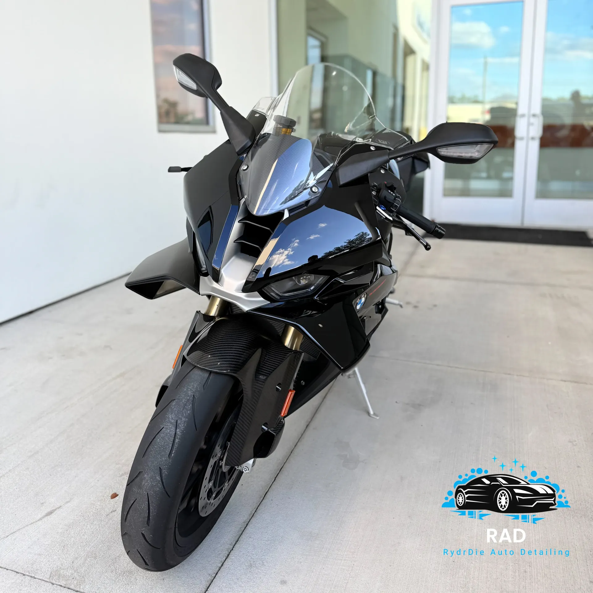 A glossy black sportbike parked on a concrete surface in front of a white building with glass doors.