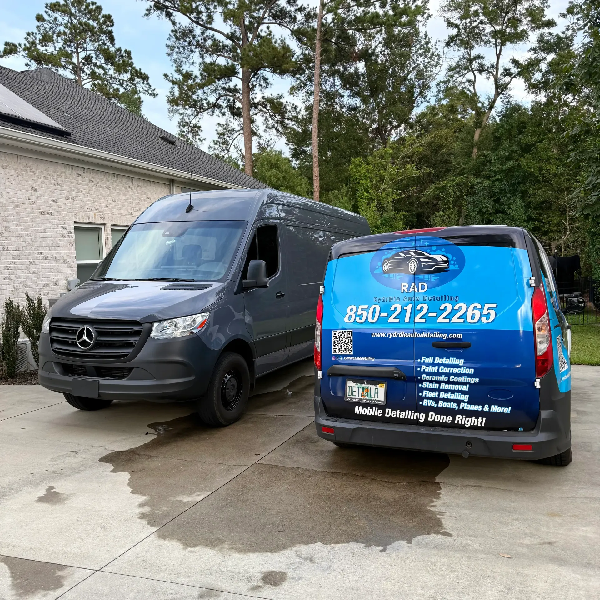 A mobile detailing van parked next to a car covered in thick white soap suds in an outdoor lot.