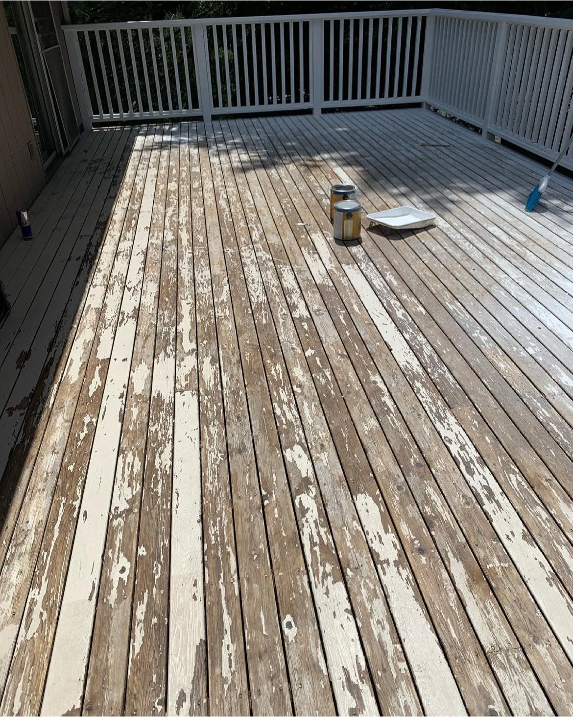 A weathered wooden deck with peeling white paint. Paint cans and a brush are visible.