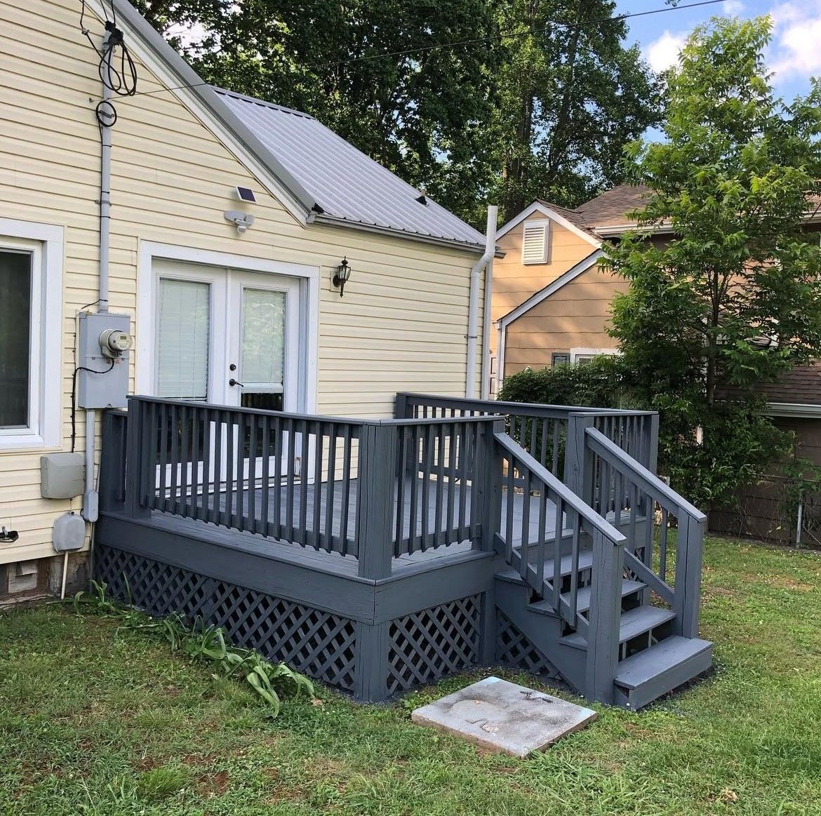 Gray wooden deck attached to a yellow house with a grassy yard.