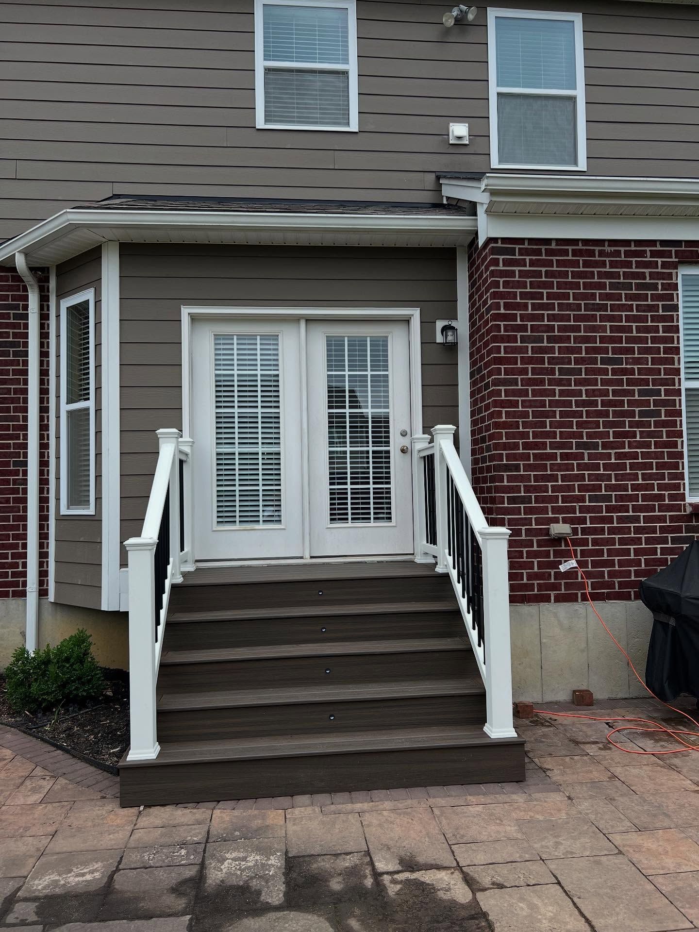 Backyard with brick and wood siding, steps leading to double doors. White railing, patio.