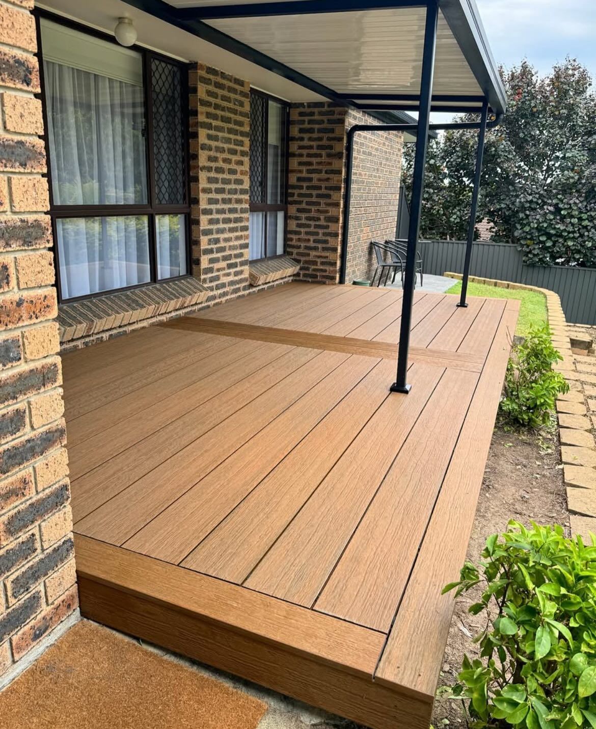 Wooden deck with a covered area outside a brick house.