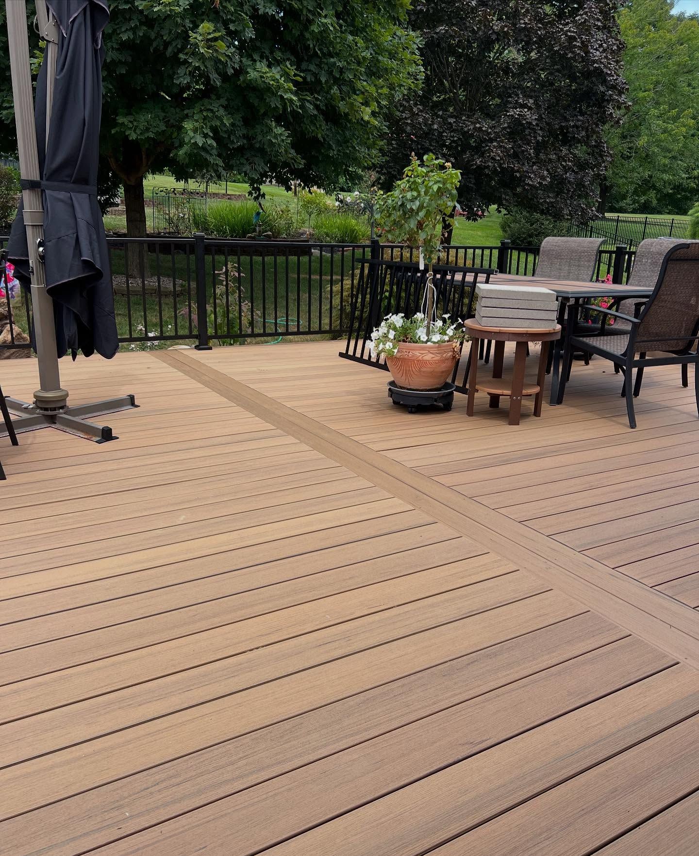 Wooden deck with patio furniture, potted plants, and black railing against a garden.