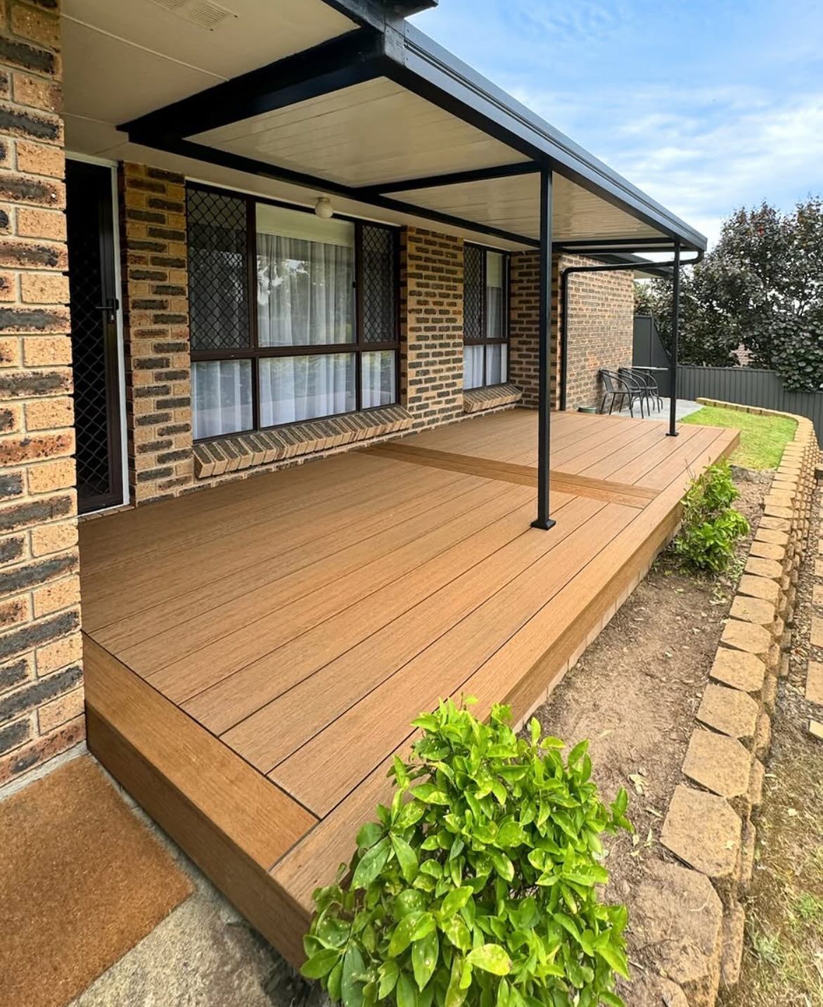 Wooden deck with black awning, brick house, and landscaping.