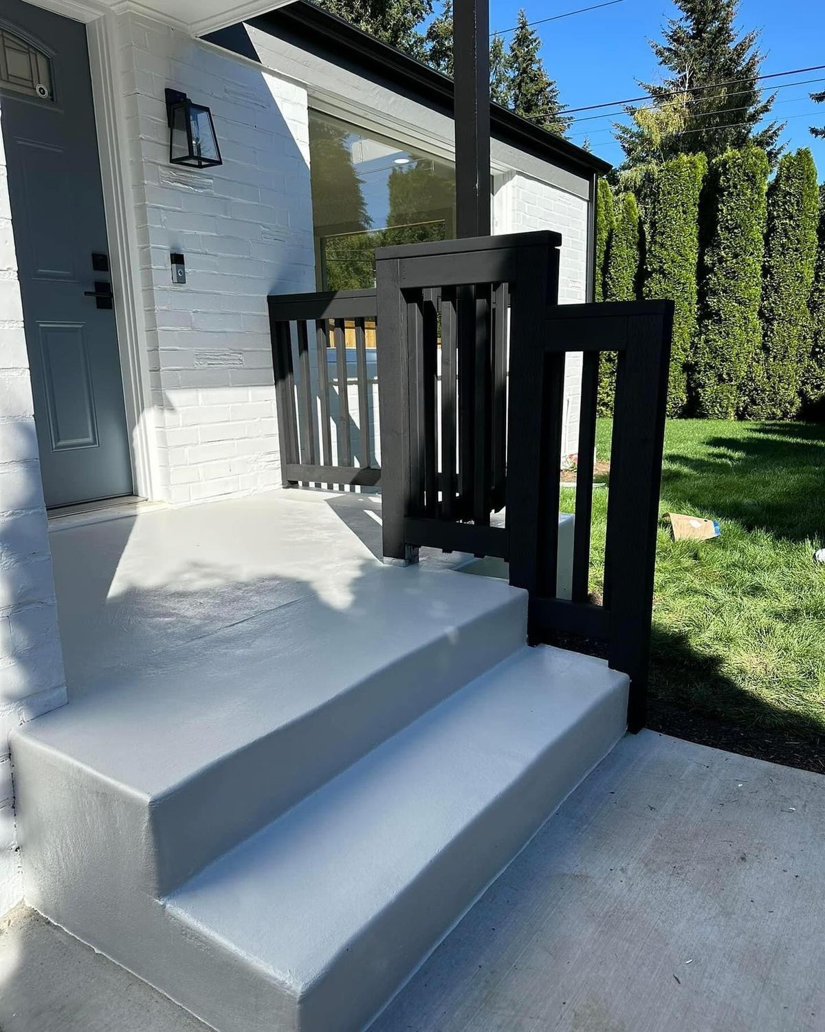 Gray concrete steps with black railing leading to a white house with black trim.