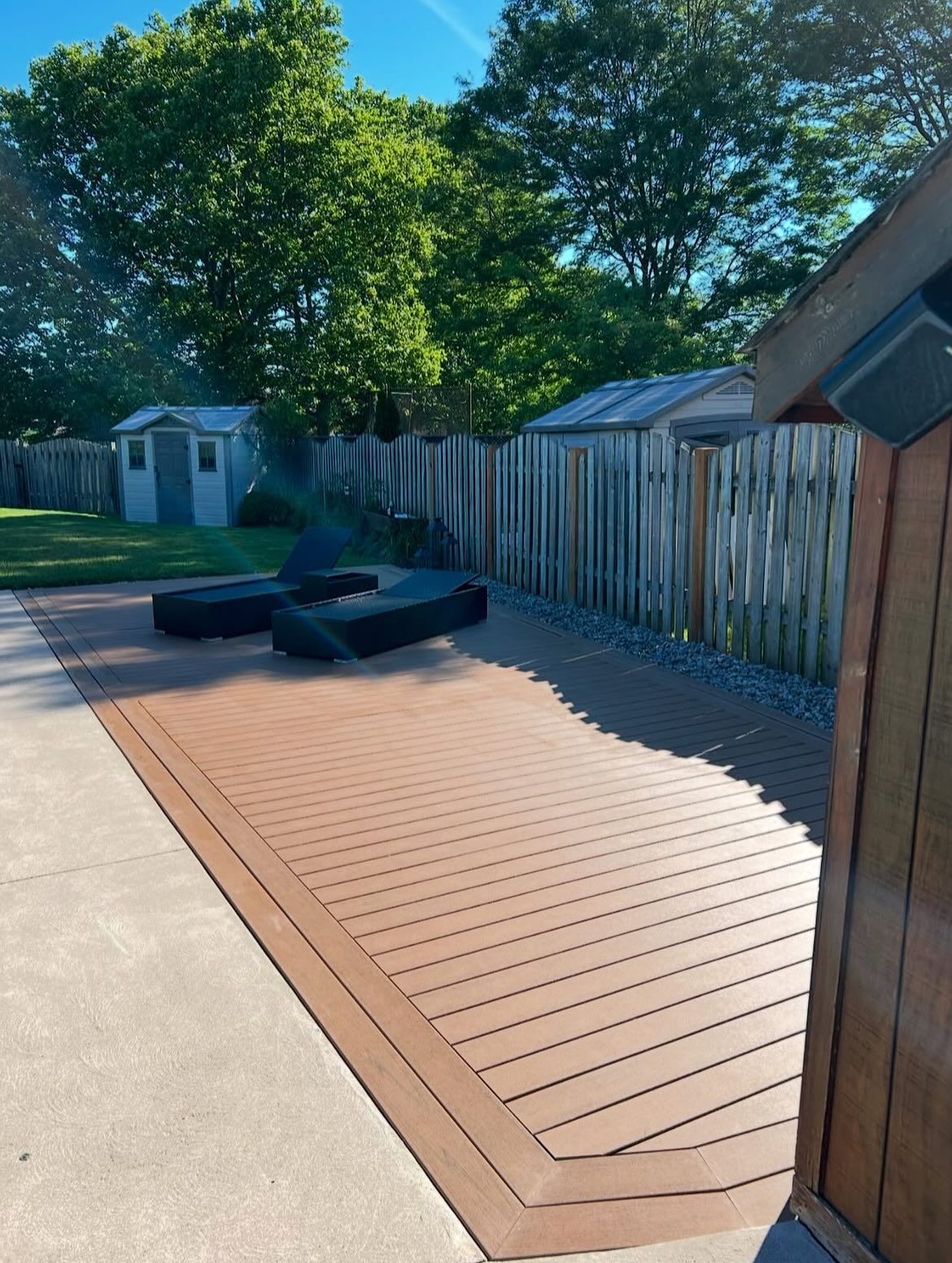 Brown composite deck, fire pit, and fence in a backyard on a sunny day.