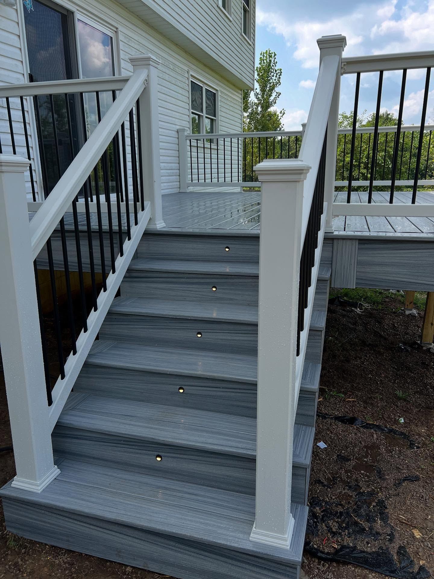 Outdoor deck stairs with gray composite steps, white posts, and black railings.