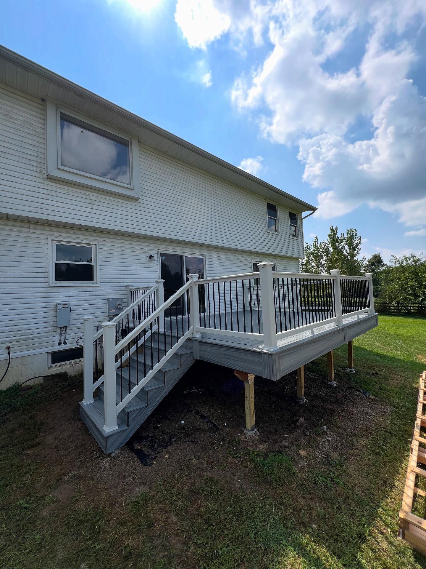 Gray and white deck with black railing attached to a two-story house on a sunny day.