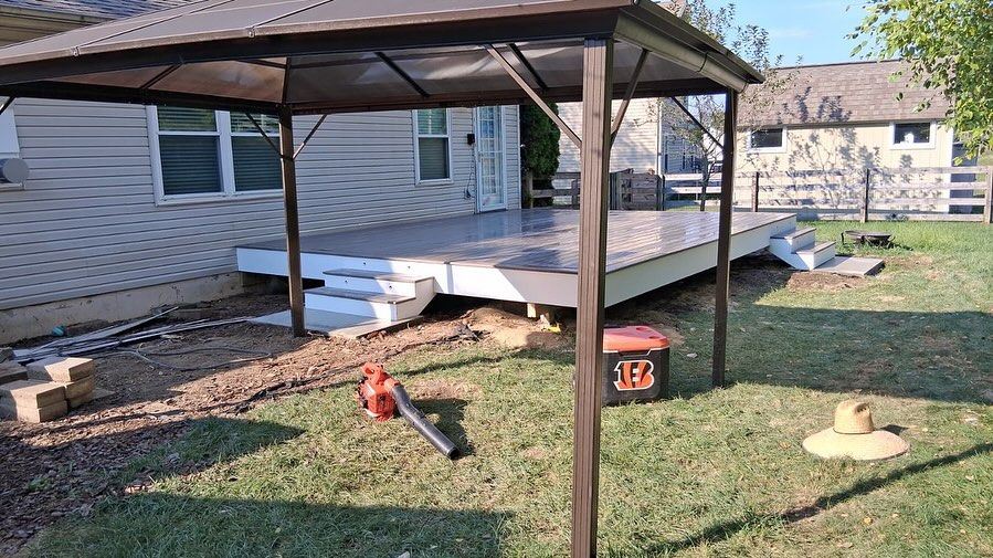 Backyard deck with gazebo, grass lawn, house in background, tools and hat in foreground.