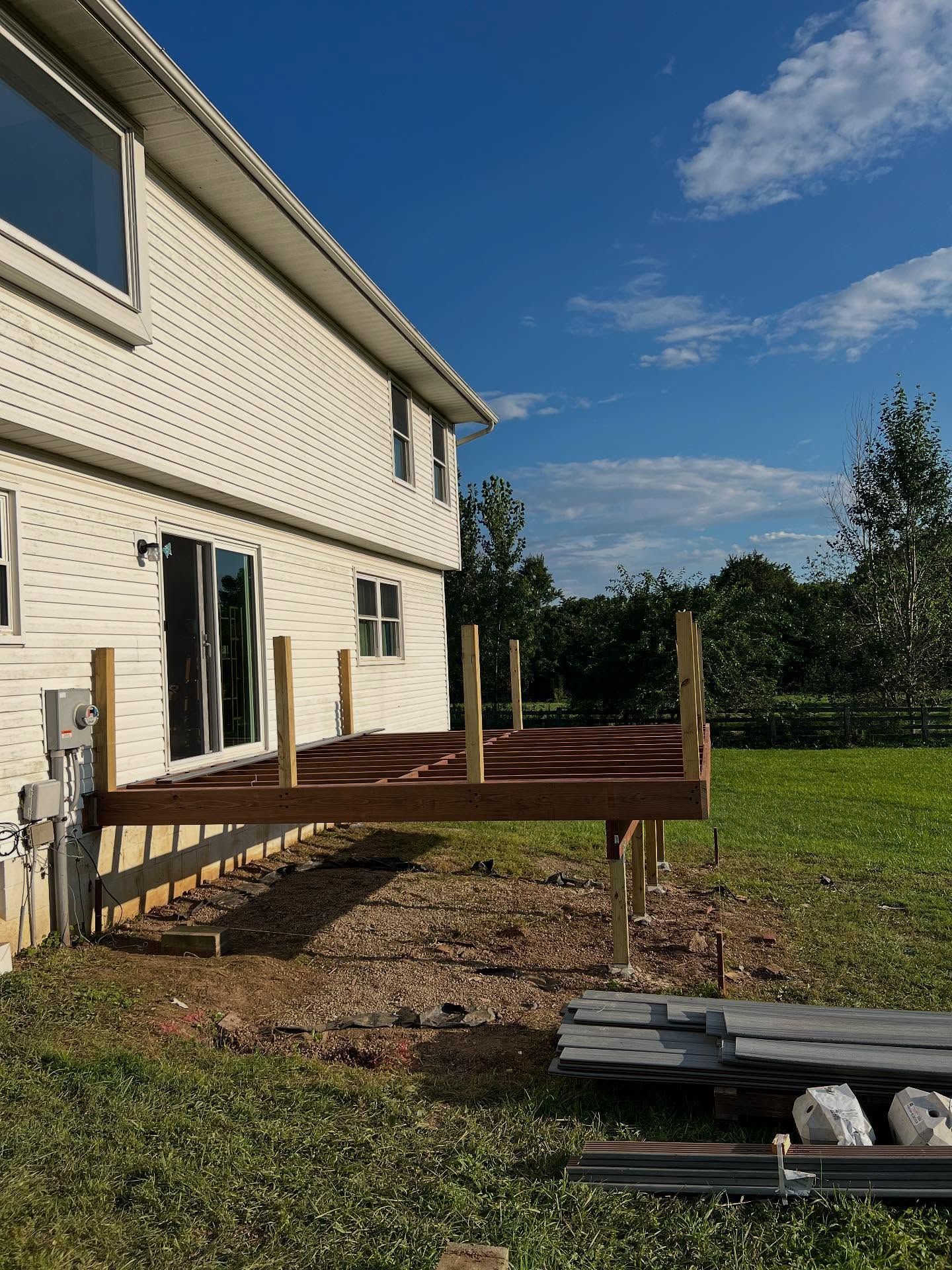 Deck construction in progress next to a white house on a sunny day.