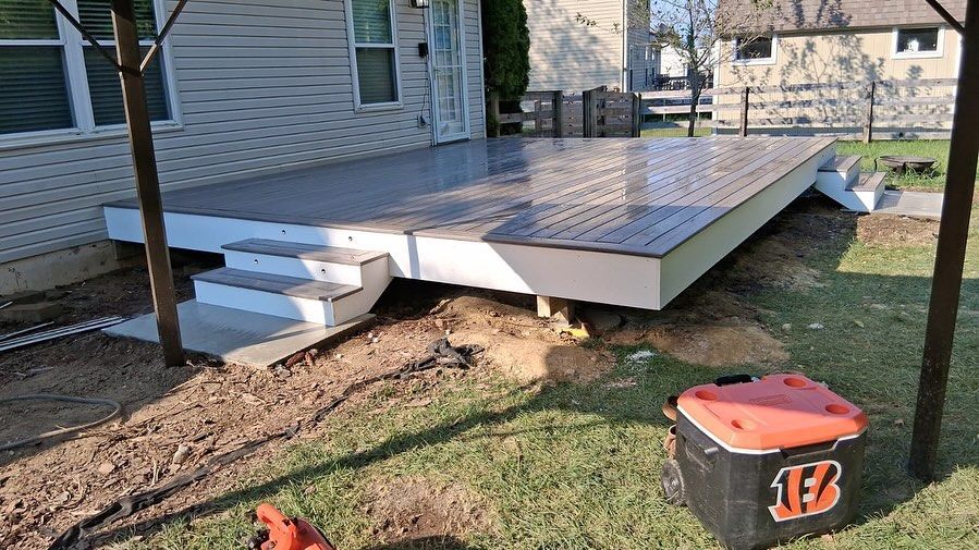Composite deck with stairs, white trim, brown composite boards, near a house and lawn, a toolbox.