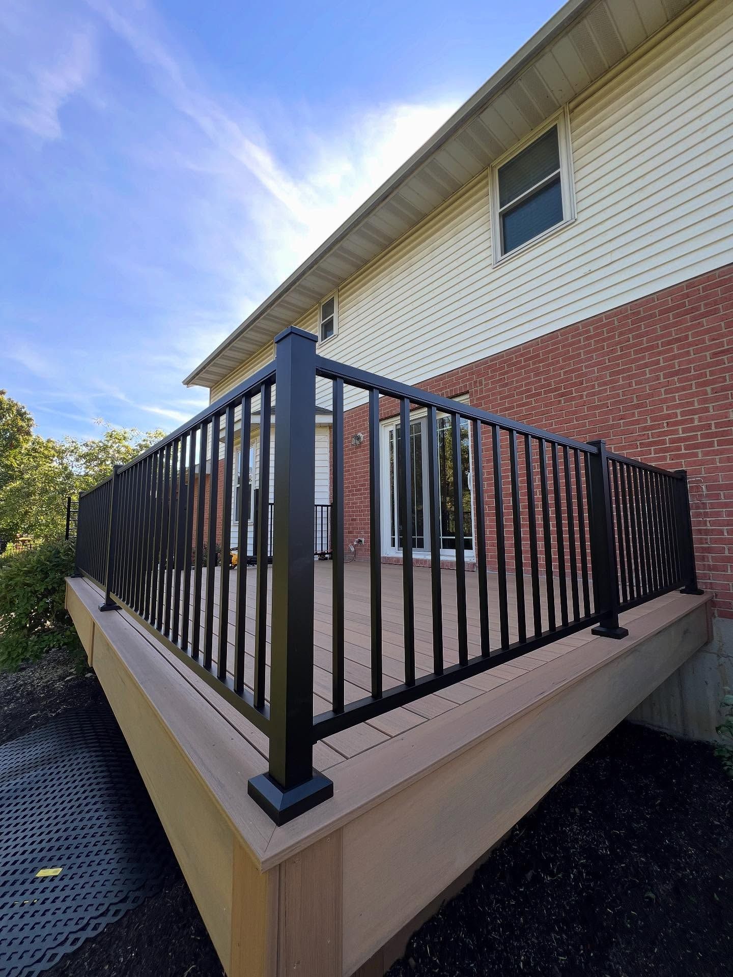 Black railing on a wooden deck attached to a brick house, with clear skies visible.