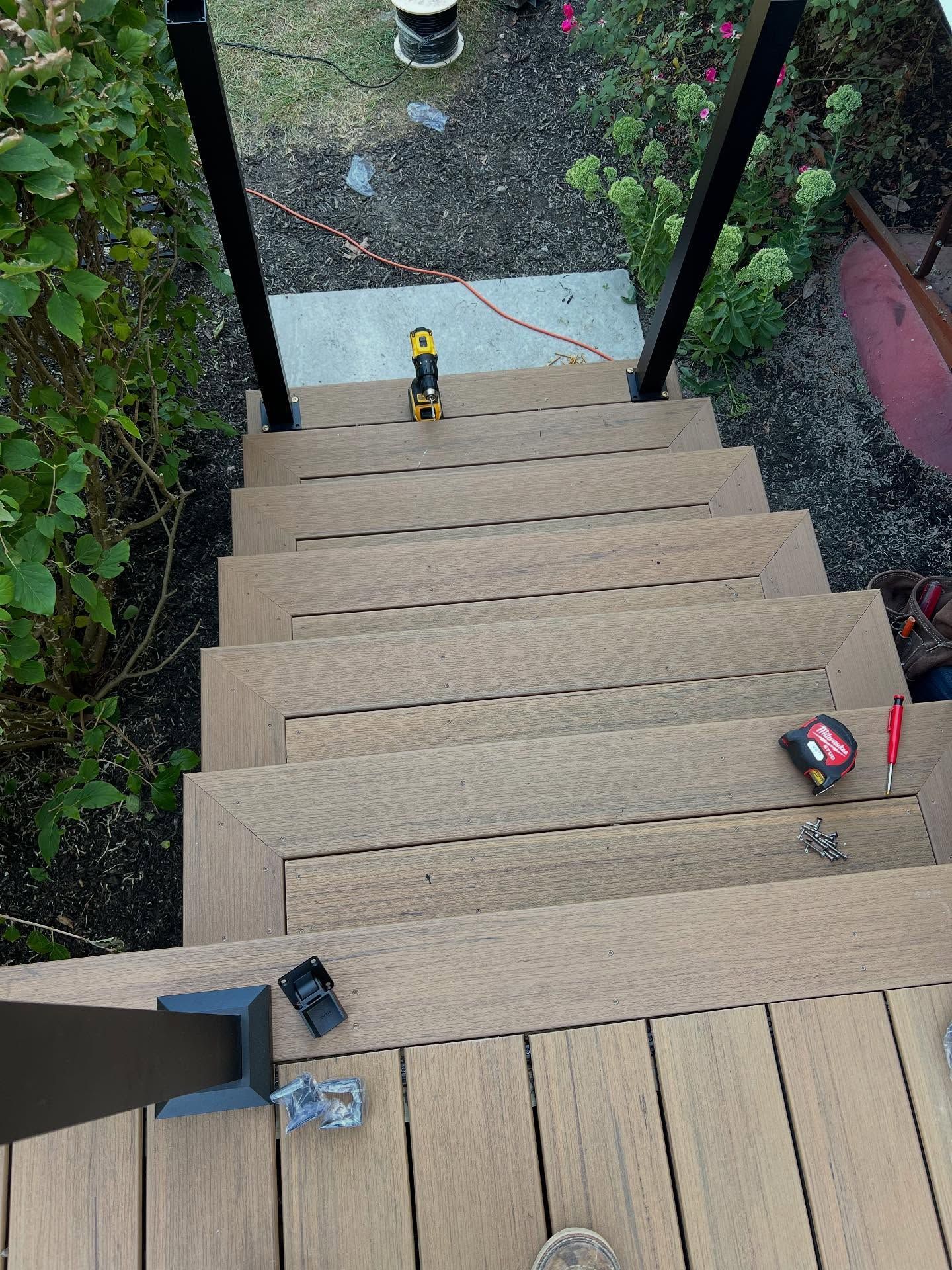 Staircase with light brown composite treads and dark metal railings. Tools are scattered on the steps.