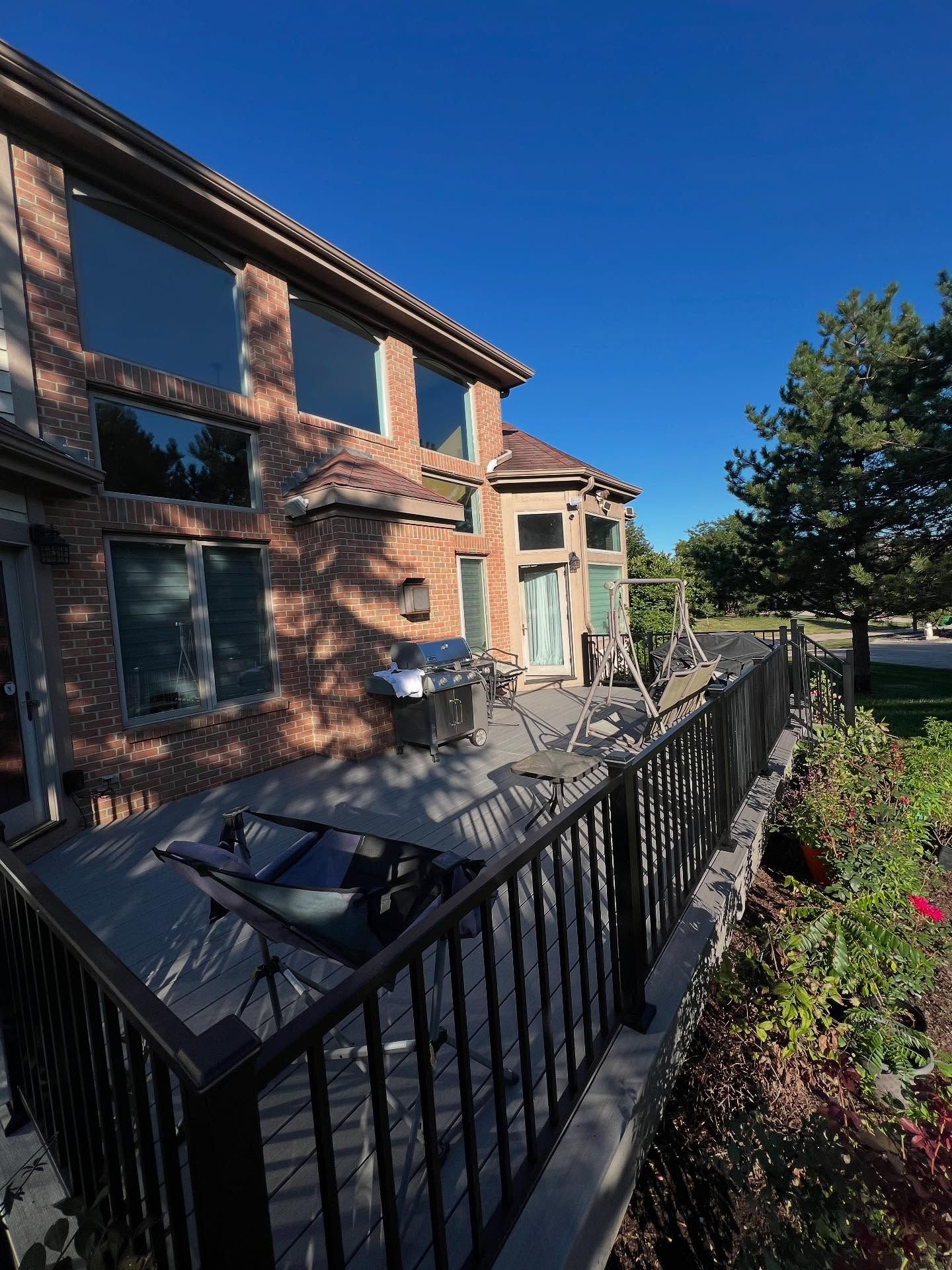 A two-story brick house with a composite deck, black railing, and grill on a sunny day.
