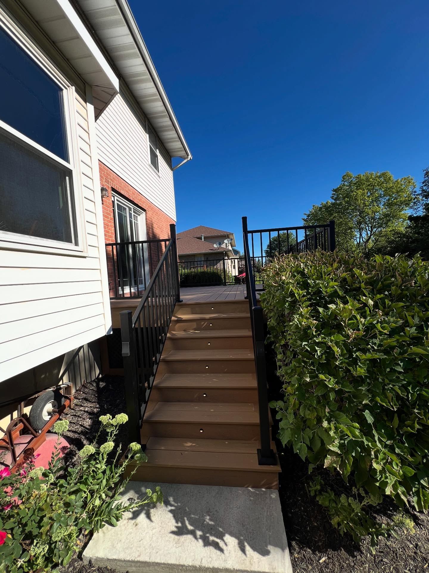 Wooden deck with steps, black railings, and a house exterior under a clear blue sky.