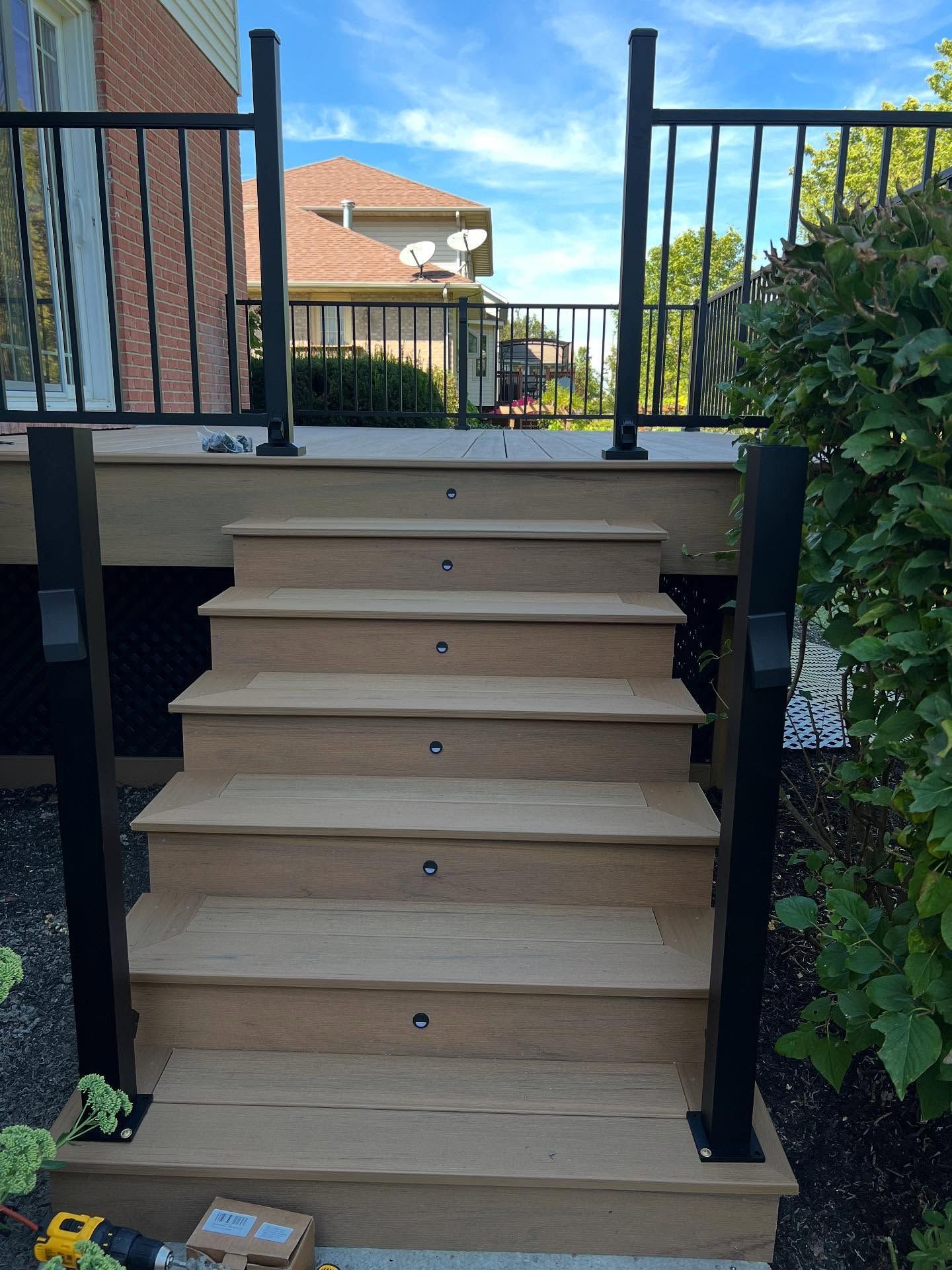 Wooden deck stairs with built-in lights, black posts, and a black railing, leading up to a deck.