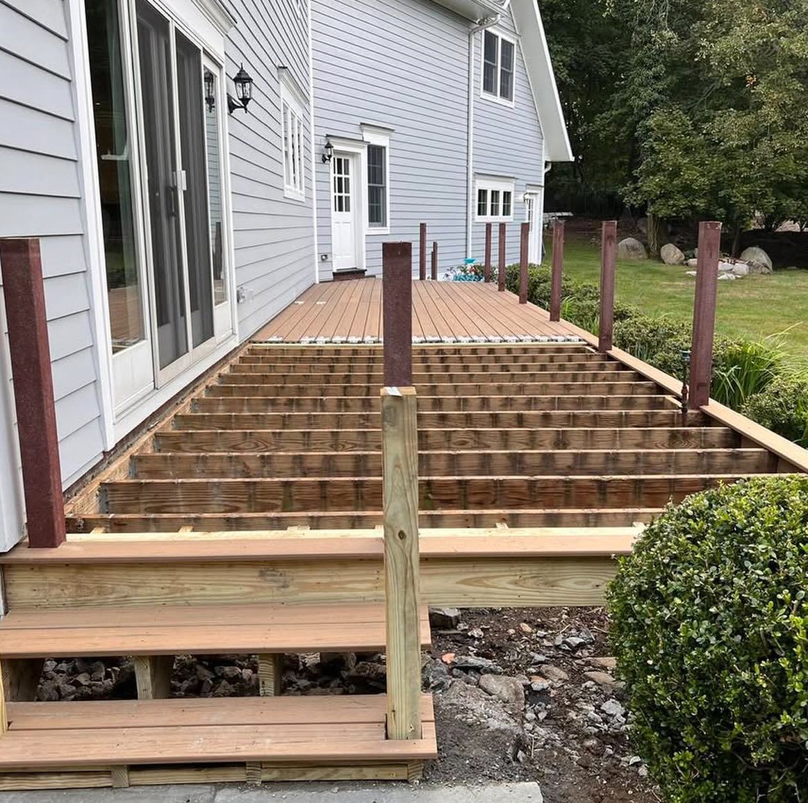 Deck under construction outside a light blue house; brown wood frame and posts.