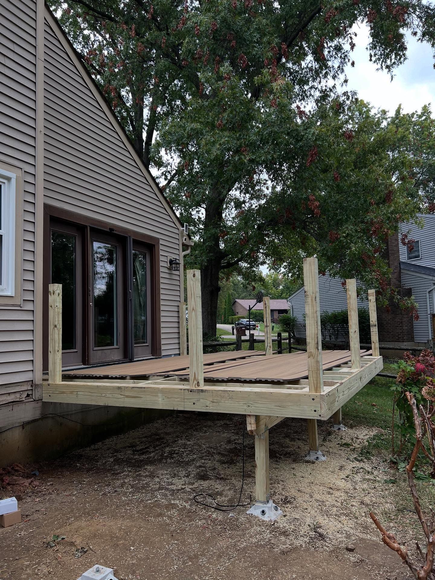 Partially built wooden deck attached to a house, supported by concrete pillars.